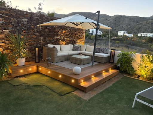 Tarima de Ipe Terraza con sofá, sombrilla, plantas y iluminación suave, con vistas a las montañas.