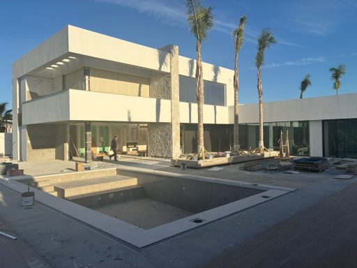 Casa moderna de dos plantas en construcción, con palmeras y piscina vacía.